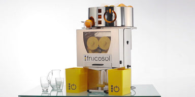 Frucosol F50A Juicer angled front facing view, the unit has oranges ready to be made to extract juice and there is a glass filling up with orange juice.
