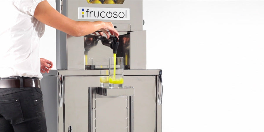 Person using a Frucosol Self-Service Juice machine to extract juice from fruits.