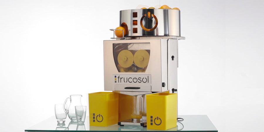 Frucosol F50A Juicer angled front facing view, the unit has oranges ready to be made to extract juice and there is a glass filling up with orange juice.