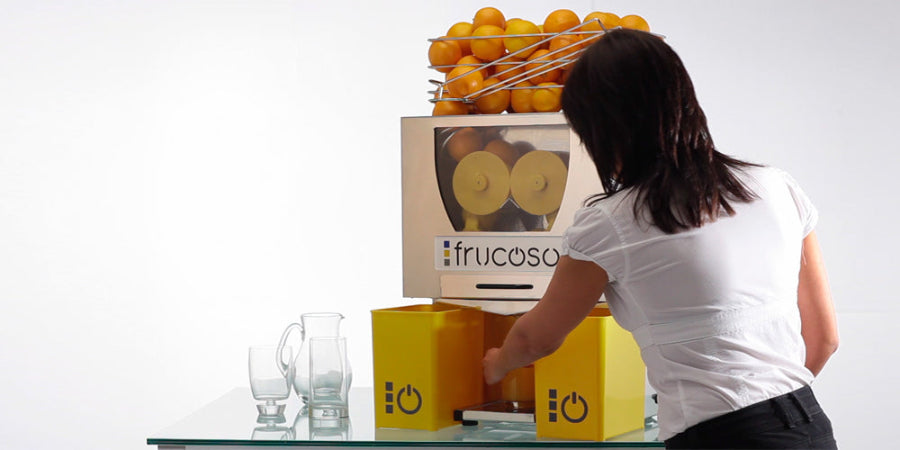 Person operating a Frucosol F50 Juicer, filling their glass with orange juice.