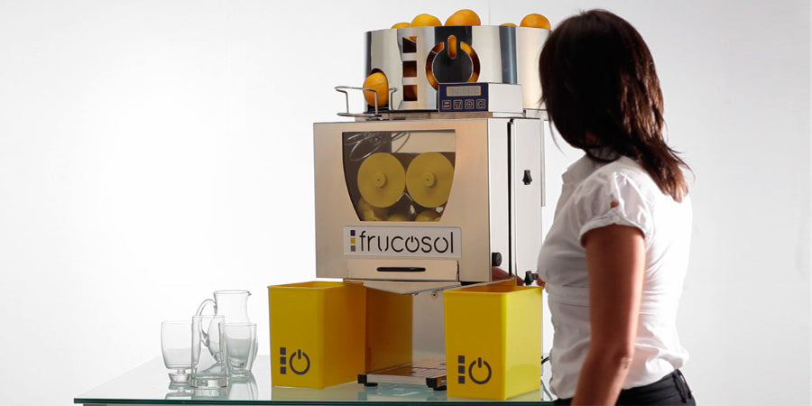 Person walking by a Frucosol F50AC Juicer with oranges on top, on a white background.